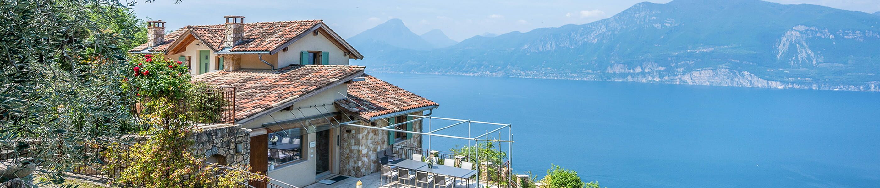 Rustikales Steinhaus mit Ziegeldach an einem blauen See in Venetien mit Bergpanorama