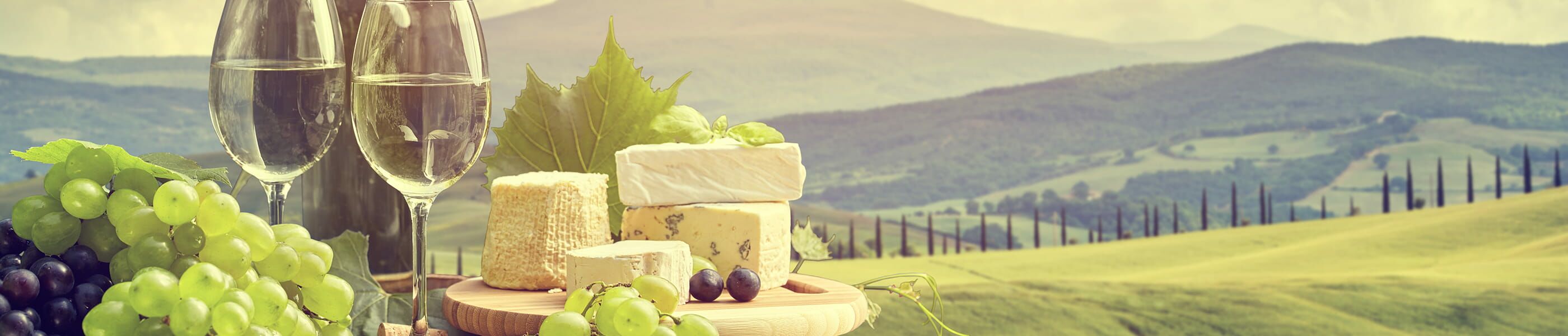 Weißwein, Trauben und Käse vor toskanischer Hügellandschaft – Weinproben in der Toskana erleben