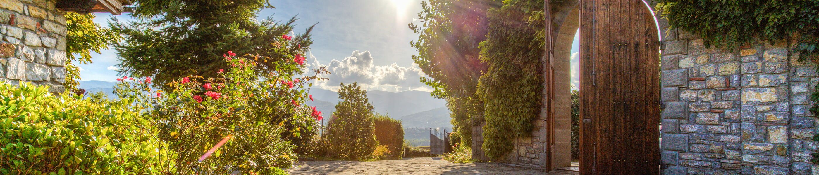 Rustikales Eingangstor einer Toskana-Finca mit Blumengarten und Sonnenlicht im Sommer